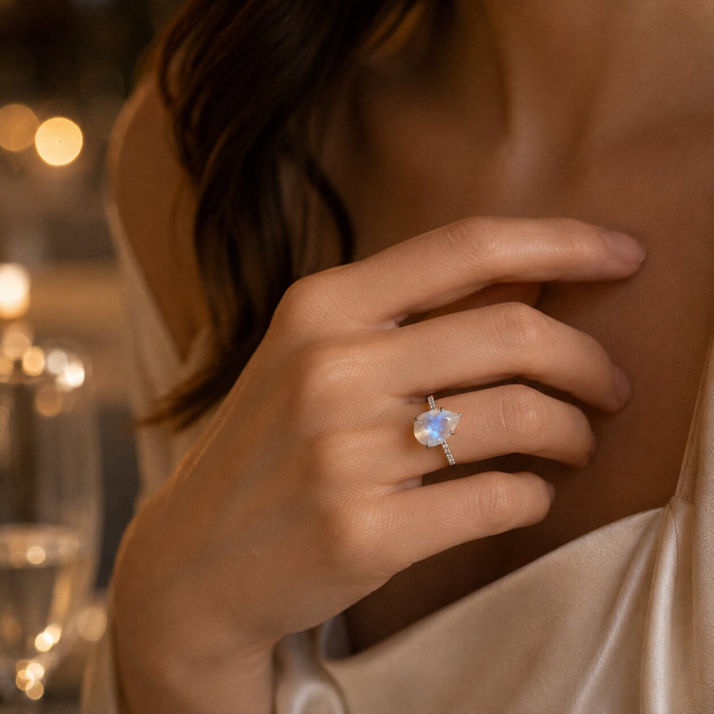Lunelle pear-shaped moonstone ring worn on a hand in warm evening light, showcasing its delicate sparkling band and blue iridescent stone