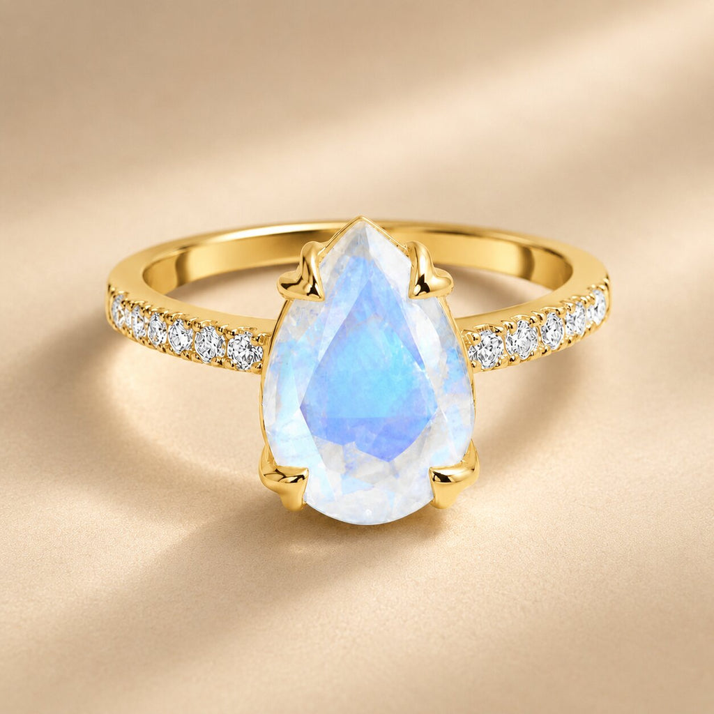 Lunelle pear-shaped moonstone ring in gold with sparkling side stones on a warm ivory background