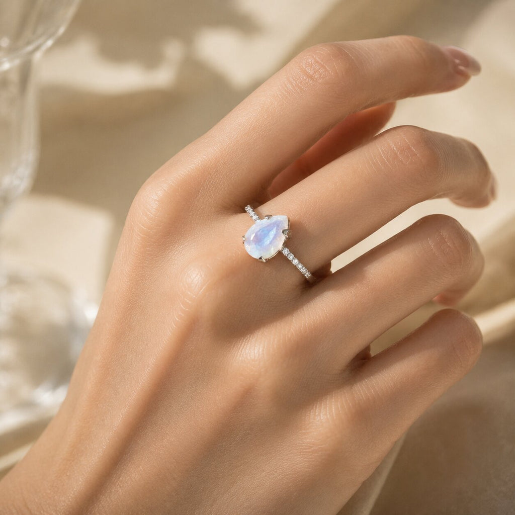 Lunelle pear-shaped moonstone ring worn on a hand, featuring a delicate band with sparkling side stones and soft blue iridescent flashes