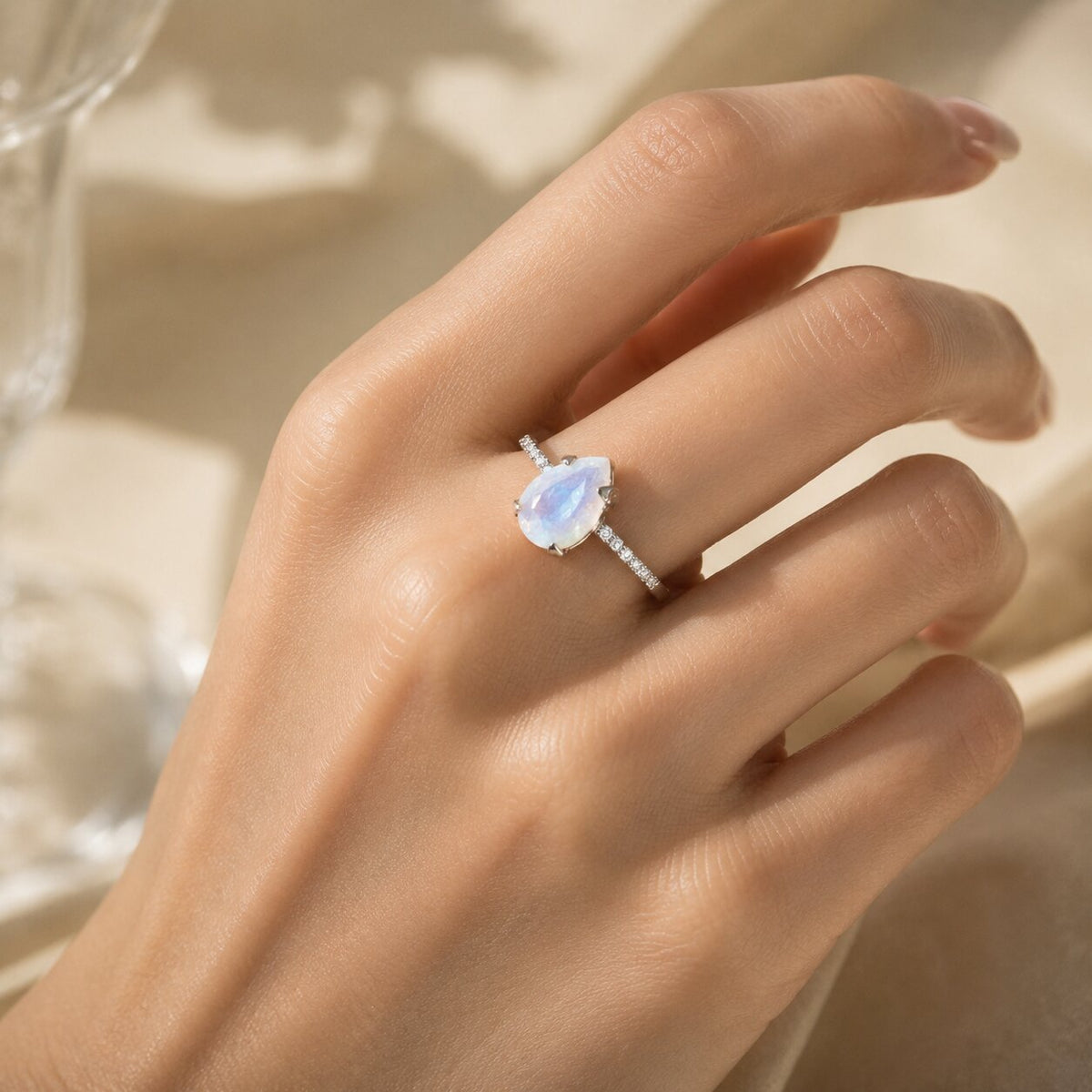 Lunelle pear-shaped moonstone ring worn on a hand, featuring a delicate band with sparkling side stones and soft blue iridescent flashes