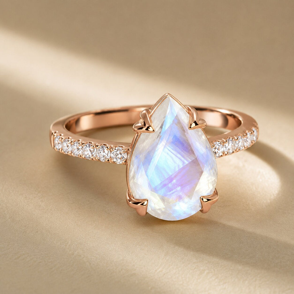 Close-up of the Lunelle pear-shaped moonstone ring in rose gold with iridescent blue and lavender flashes and sparkling side stones