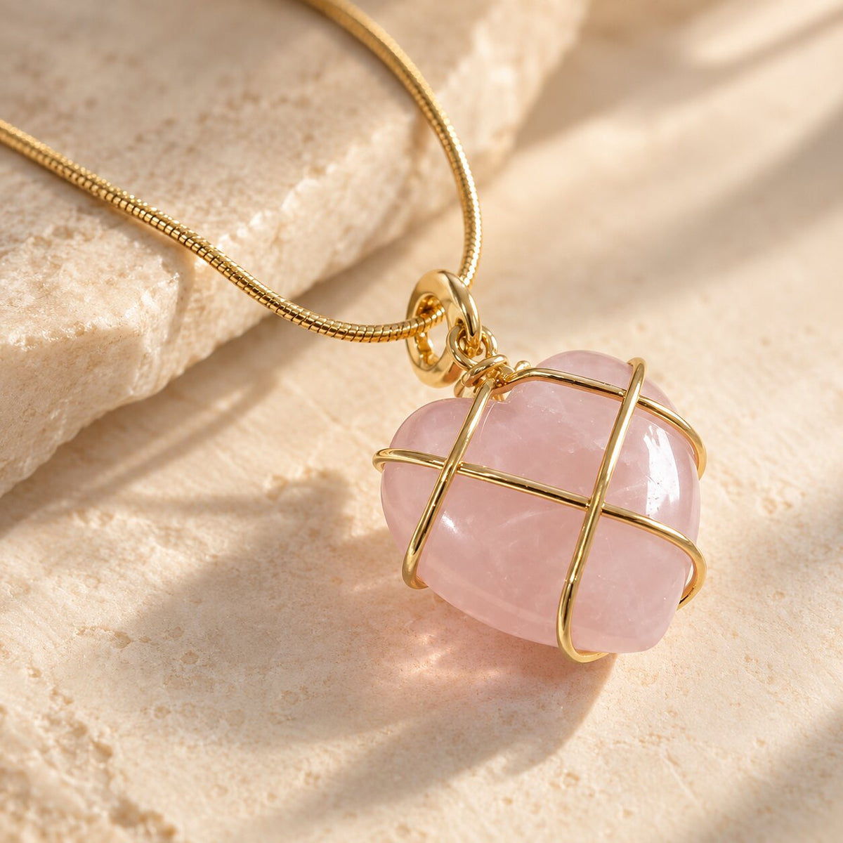 Close-up of the Caelisse Moonstone Heart Necklace featuring a polished pastel pink gemstone pendant with delicate gold wire wrapping and a fine gold chain.